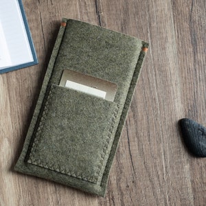 May include: An olive green felt sleeve case featuring a rectangular front pocket with visible stitching along the edges. A metallic gold card is partially inserted into the pocket. The sleeve has small orange thread accents at the top corners.