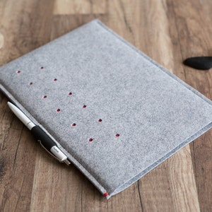 May include: A grey felt laptop sleeve with red stitching and a pen sticking out of the side.