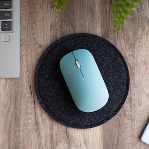 May include: A light blue wireless mouse on a black circular mousepad. The mousepad is on a wooden surface.