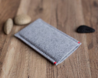 May include: A rectangular light gray felt sleeve case with a soft, textured surface. The sleeve features visible stitching along the edges, with two small, distinct red thread accents at the opening, providing a subtle contrast to the gray felt.