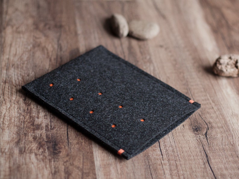 May include: A dark gray felt case with orange stitching. The case has a series of small holes throughout the surface.