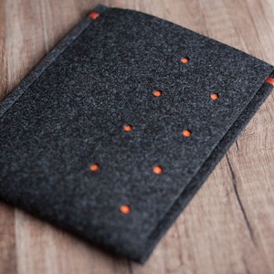 May include: A gray felt laptop sleeve with orange stitching and a pattern of evenly spaced holes.
