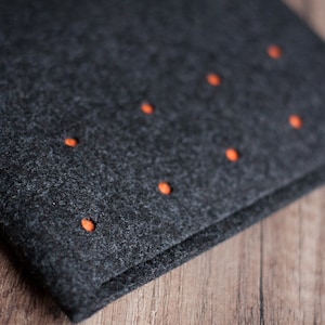 May include: A dark gray felt pouch with orange stitching. The pouch has a fold-over flap and is closed with a snap.