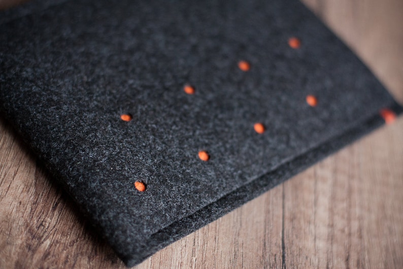 May include: A dark gray felt pouch with orange stitching. The pouch has a fold-over flap and is closed with a snap.