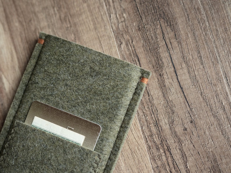 May include: An olive green felt card holder featuring a rectangular pocket with visible stitching and orange thread accents at the top corners. A metallic gold credit card with a geometric pattern is partially inserted into the front pocket.