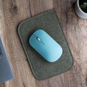 May include: A light blue wireless computer mouse on a green felt mouse mat. The mouse mat is on a wooden surface.