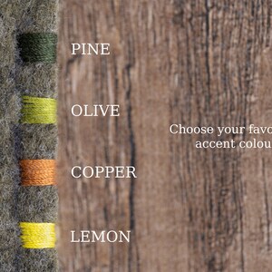May include: A textured gray felt fabric swatch featuring four vertical thread color options labeled Pine, Olive, Copper, and Lemon. The text Choose your favourite accent colour is displayed to the right of the thread samples on a wood grain background.