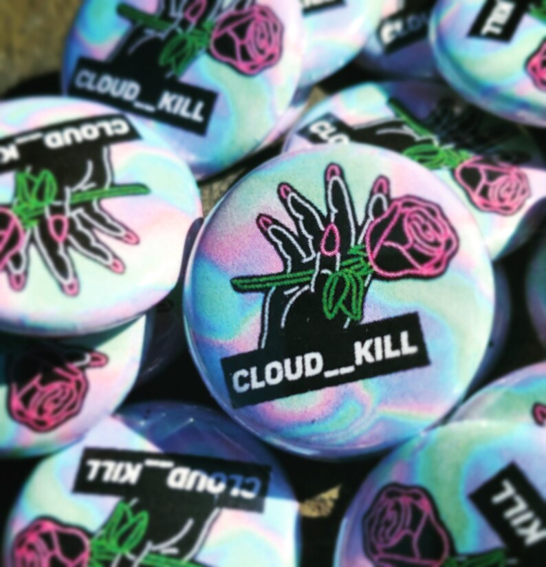 Op de afbeelding: Een verzameling iriserende holografische knopen met een zwart-witte afbeelding van een hand die een roze roos vasthoudt en de tekst "CLOUD_KILL".
