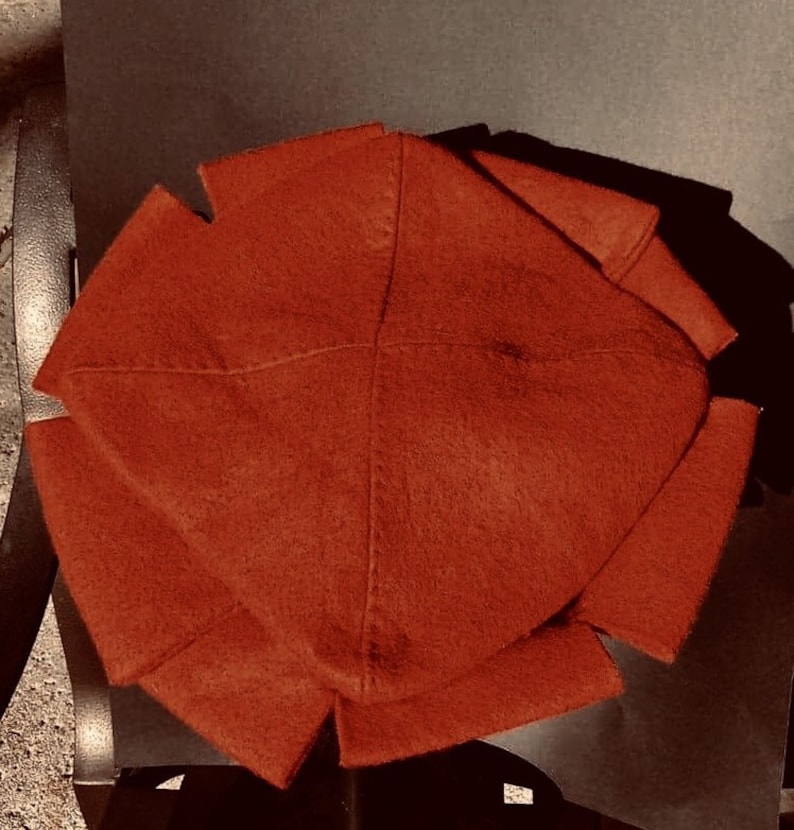 May include: A rust-colored felt hat with a unique, folded design. The hat is folded into eight sections, creating a geometric pattern.