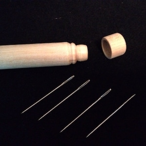 Może przedstawiać: Drewniane pudełko na igły z pokrywką, otwarte, aby ukazać pięć srebrnych igieł.