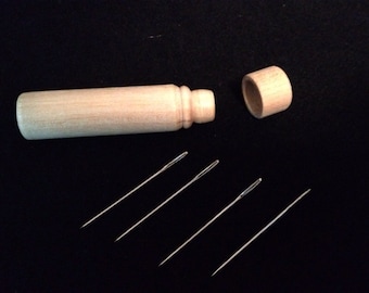 Puede incluir: Un estuche de madera para agujas con tapa, abierto para revelar cinco agujas plateadas.