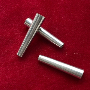 May include: Three silver metal tapered tubes on a red background.