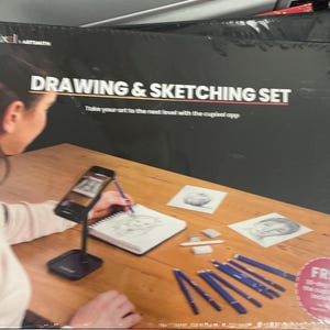May include: A black box set labeled "DRAWING & SKETCHING SET" with the "cupixel artsmith" logo. The set includes drawing pencils, a sketchbook, and a phone stand. The text on the box says "Take your art to the next level with the cupixel app."