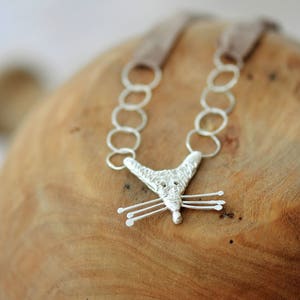 Puede incluir: Un collar de plata con un colgante de zorro y un cordón de cuero marrón. El colgante de zorro tiene una superficie texturizada y una cola larga y delgada.