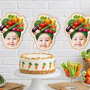 May include: A festive party scene with a baby-themed banner and a carrot-decorated cake. Fresh vegetables, including tomatoes, cucumbers, and carrots, are arranged on plates and in glasses. A basket of vegetables and balloons complete the cheerful setting.