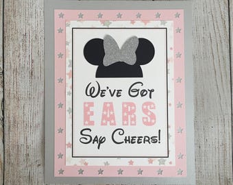 May include: A pink and gray card with a black silhouette of Mickey Mouse ears with a silver bow. The card says "We've Got Ears Say Cheers!" with pink stars around the border.