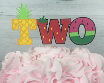 May include: A cake topper for a second birthday party, featuring the word "TWO" decorated with a pineapple, strawberry, and watermelon design.