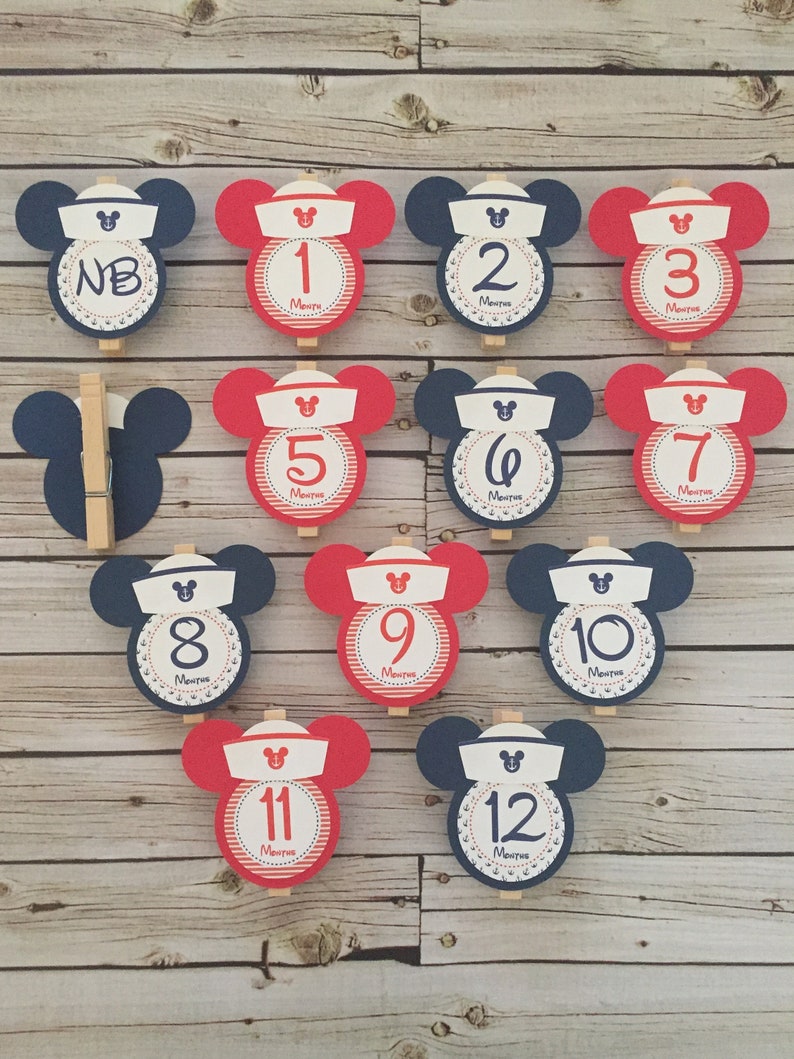 May include: Twelve red and blue Mickey Mouse themed monthly milestone cards with a sailor hat and anchor design. The cards are numbered from NB to 12 months.
