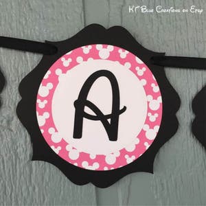 Op de afbeelding: Zwart-witte banner met een roze en wit Mickey Mouse-patroon. De letter "A" staat in het midden van de banner.