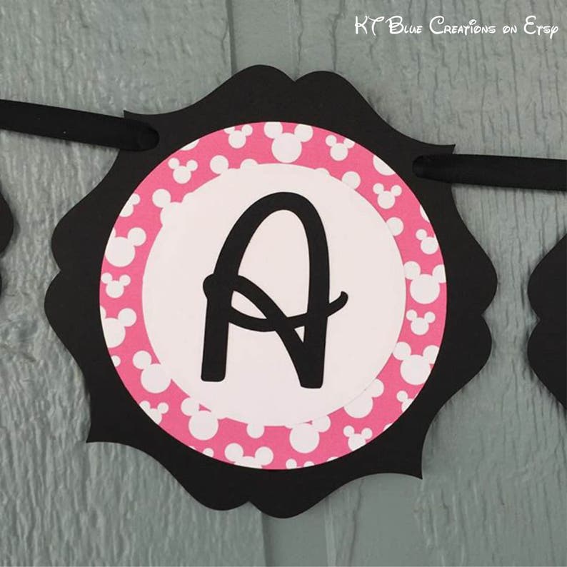 Op de afbeelding: Zwart-witte banner met een roze en wit Mickey Mouse-patroon. De letter "A" staat in het midden van de banner.