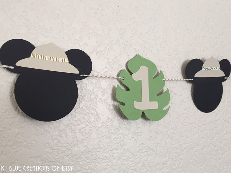 Puede incluir: Una pancarta de Mickey Mouse en blanco y negro con hojas verdes y el n&uacute;mero uno. La pancarta es perfecta para una fiesta de primer cumplea&ntilde;os.