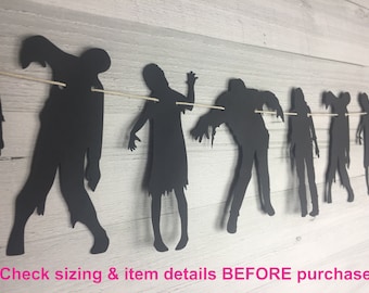 May include: Black paper zombie silhouette banner with 8 zombies in different poses. The banner is strung with white twine.