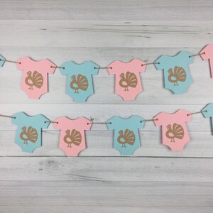 May include: A gender neutral baby shower banner with alternating pink and blue baby onesies with a gold turkey graphic on each onesie.