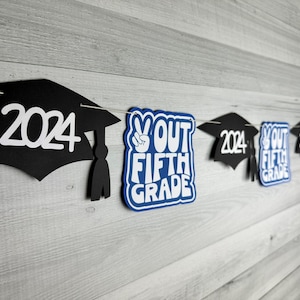 May include: A graduation banner with black graduation caps and blue and white "Out Fifth Grade" signs. The caps have the year 2024 printed on them.