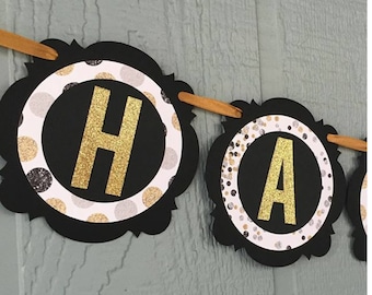 Könnte beinhalten: Schwarz-weißes Banner mit goldenen Glitzerbuchstaben, die "Happy" buchstabieren. Das Banner hat ein Punkte-Muster mit goldenen und silbernen Punkten.