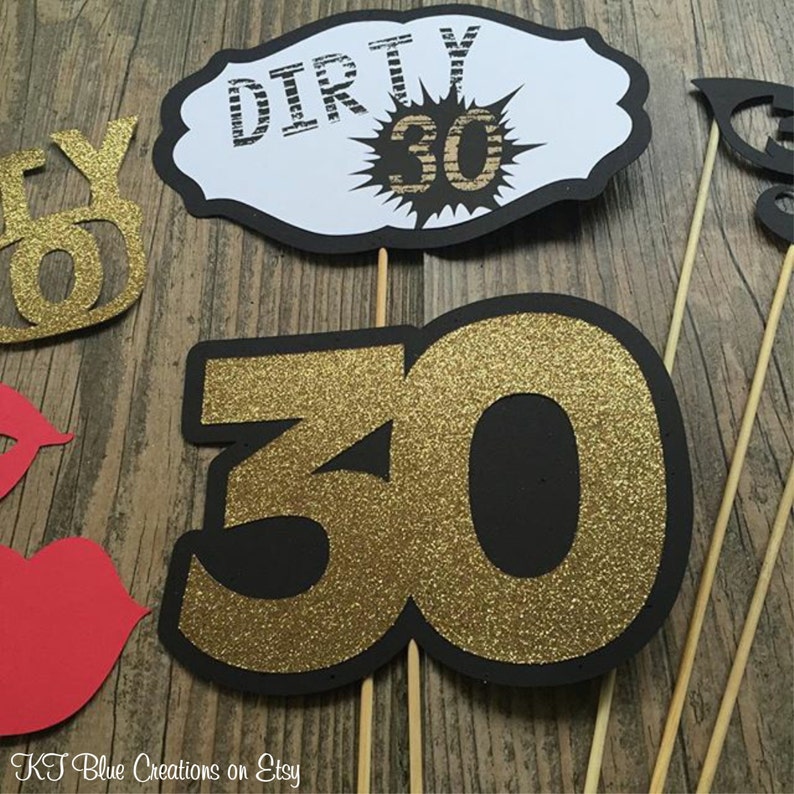 May include: A set of black and gold photo booth props for a 30th birthday party. The props include a sign that says "Dirty 30", a large number "30", and a pair of red lips.