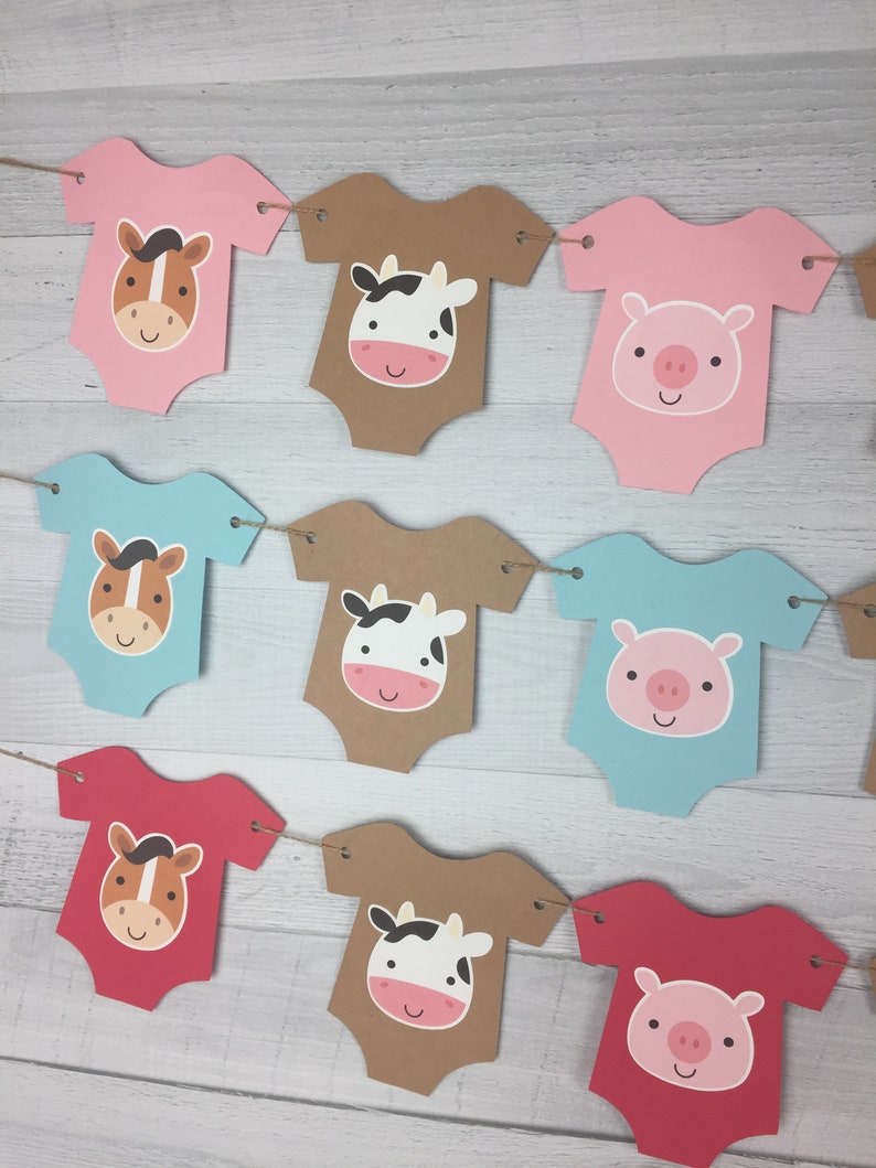 May include: A banner with nine baby onesies featuring farm animal faces. The onesies are in pink, blue, brown, and red. The animals are a horse, a cow, and a pig.