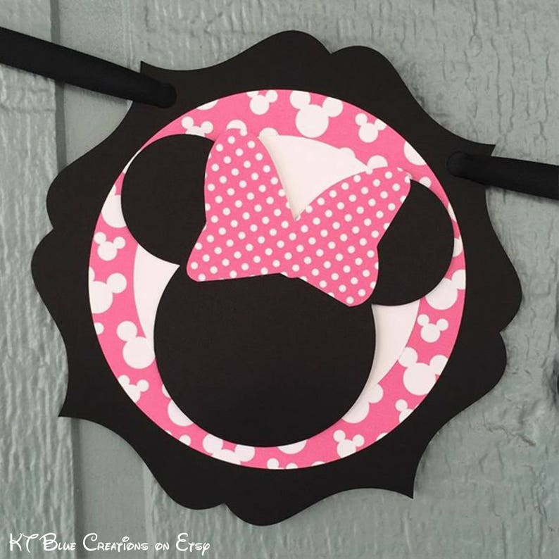 Op de afbeelding: Zwarte en roze Minnie Mouse-personagebanner met witte stippen. De banner heeft de vorm van een cirkel met een gegolfde rand.