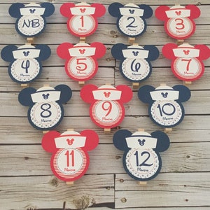 May include: Twelve red and blue Mickey Mouse-themed monthly milestone cards with white numbers and the word "Months" printed on each card. The cards are decorated with white anchors and red and white stripes.