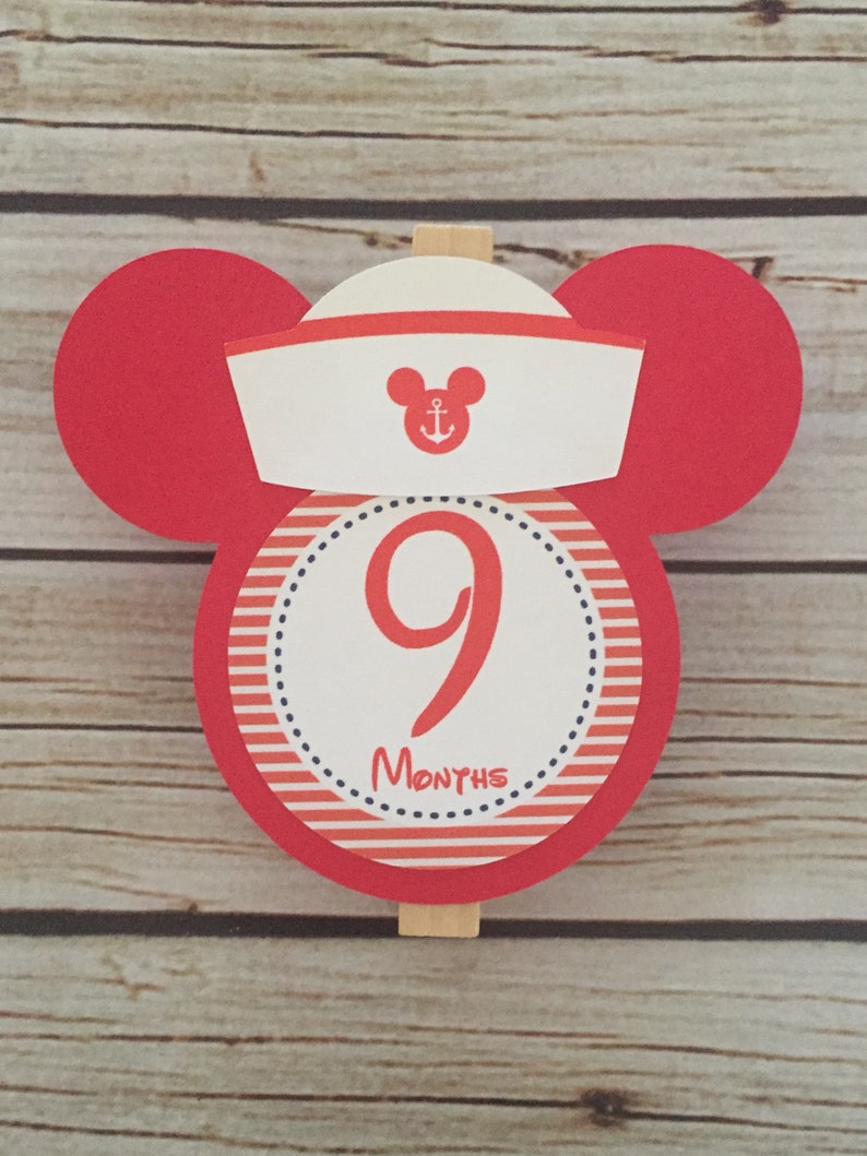 May include: Red and white Mickey Mouse themed monthly milestone marker with a white sailor hat, an anchor, and the number 9. The text "MONTHS" is printed below the number.