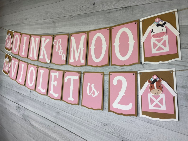 May include: Pink and brown banner with the text "OINK  BAA  MOO  VIOLET is 2" with a cow and a horse in a barn illustration on each end.
