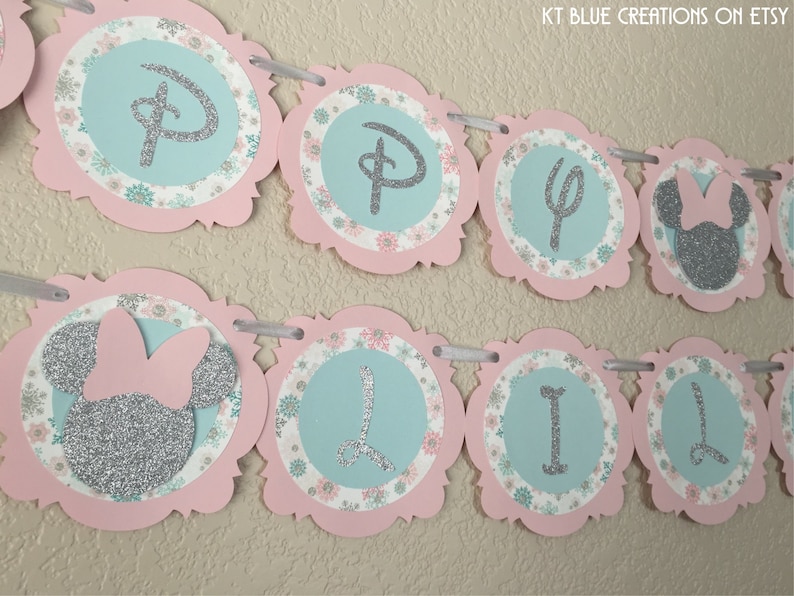 May include: A pink and blue banner with silver glitter letters and a silver glitter Minnie Mouse head. The banner says "Happy 1st Birthday".