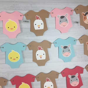 May include: A baby shower banner with a farm animal theme. The banner is made of brown, pink, blue, and red cardstock and features cutouts of baby onesies with animal faces. The animals include a chick, a chicken, and a donkey.