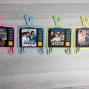 May include: A banner with five television-shaped cutouts, each featuring a different 80s TV show. The shows are "Punky Brewster", "Miami Vice", "The A-Team", "The Golden Girls", and "Diff'rent Strokes".