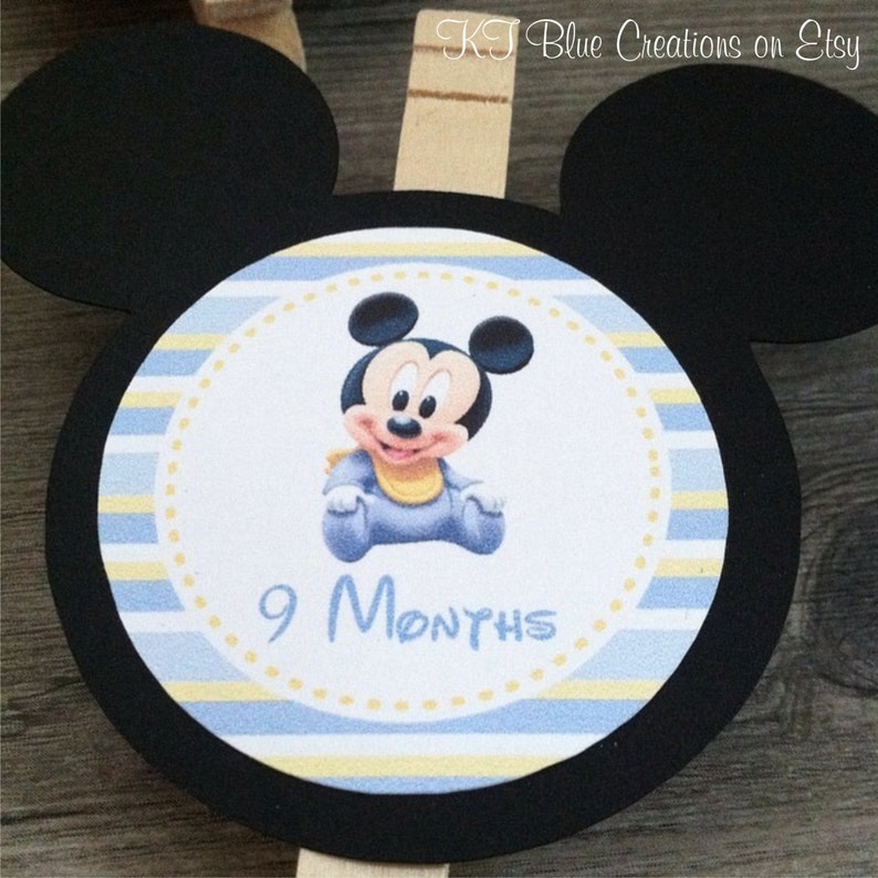 May include: Black and white Mickey Mouse character with yellow and blue striped background. The character is wearing a blue outfit and a yellow bib. The text "9 Months" is printed below the character.