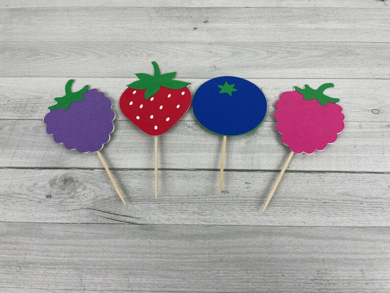 Peut inclure: Quatre d&eacute;corations de cupcakes en feutre de fruits color&eacute;s&nbsp;: une fraise rouge, une m&ucirc;re violette, une framboise rose et une myrtille bleue.