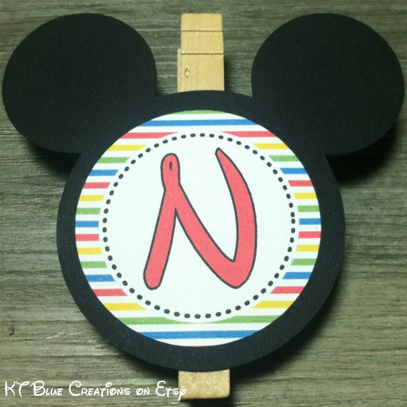 May include: Black and white Mickey Mouse-shaped card with a colorful striped circle in the center. The circle has a white background with a red letter "N" in the center. A wooden clothespin is attached to the top of the card.