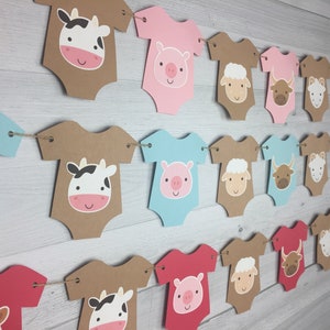 May include: A brown, pink, blue, and red banner with farm animal baby onesies. The onesies feature a cow, pig, sheep, bull, and chick. The banner is strung together with twine.