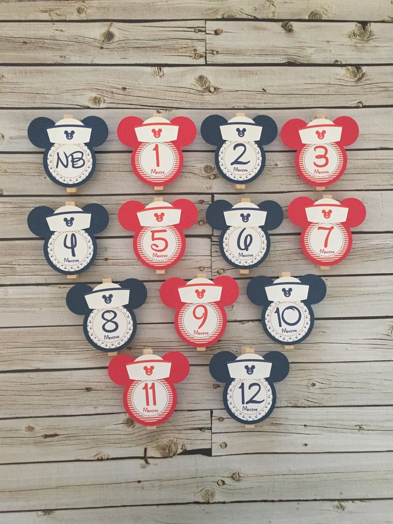 May include: Twelve red and blue Mickey Mouse-shaped cards with numbers 1 through 12 and the word "Months" printed on each card. The cards are attached to wooden clothespins.