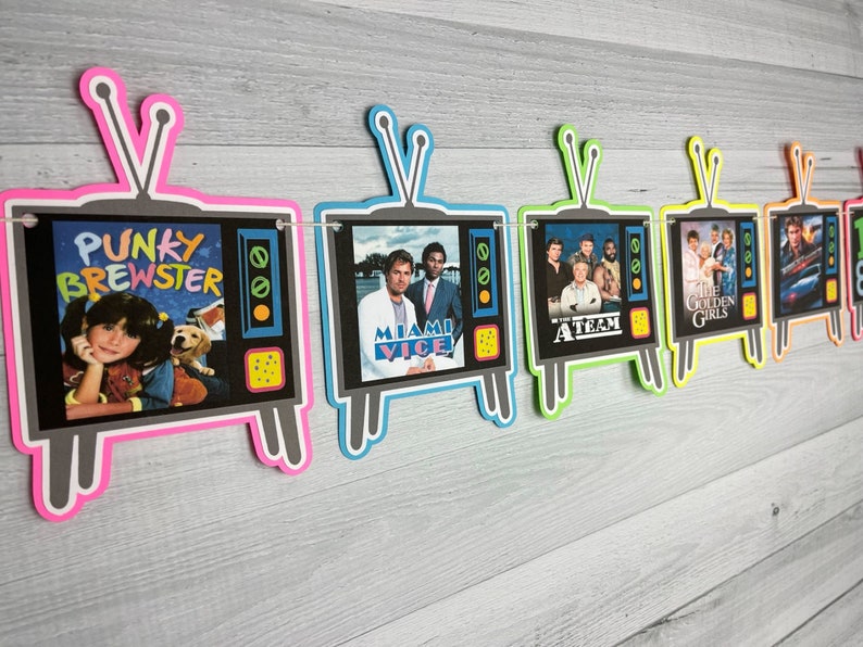 May include: A colorful banner with images of popular 80s television shows. The banner is made of cardboard and features images of "Punky Brewster", "Miami Vice", "The A-Team", "The Golden Girls", and "Knight Rider".