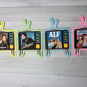 May include: A banner with five television-shaped cutouts, each featuring a different 80s television show. The shows are "Moonlighting", "21 Jump Street", "ALF", "The Facts of Life", and "The Golden Girls".