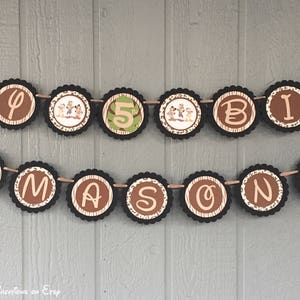 May include: A brown and tan birthday banner with the letters "Happy" and "Birthday" and the number "5" in the center. The banner is decorated with jungle animal characters and a jungle-themed pattern.