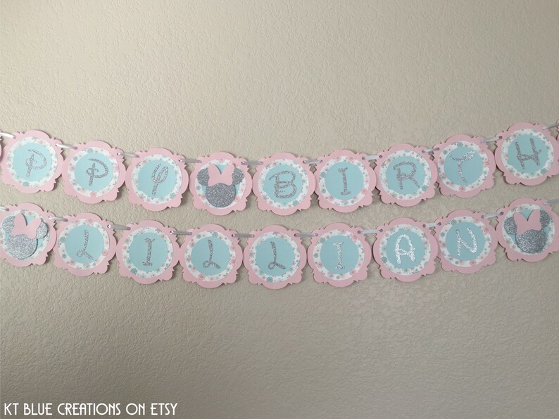 May include: A pink and blue banner with silver glitter letters spelling "Happy Birthday Lillian" with a silver glitter Minnie Mouse head on each end.