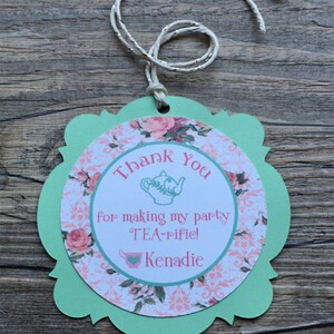 May include: A green and pink thank you tag with a teacup and teapot design. The tag says "Thank You for making my party TEA-rific! Kenadie".
