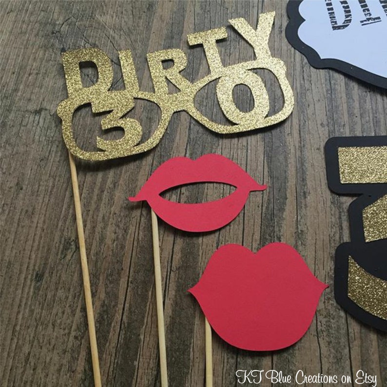 May include: A set of photo booth props for a party. The props include a pair of gold glitter glasses with the number 30, a red pair of lips, and a red pair of lips with a white outline. The props are attached to wooden sticks.