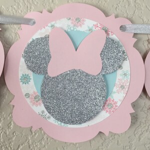 May include: Pink and silver glitter Minnie Mouse themed banner with snowflakes and a light blue background. The banner is made of cardstock and is perfect for a winter birthday party.